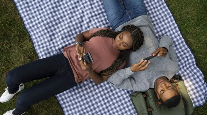 一男一女躺在野餐毯上玩手机游戏.